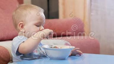 一个2岁有魅力的男孩自己在吃红汤。 勺子和手流动的液体。 健康饮食的概念